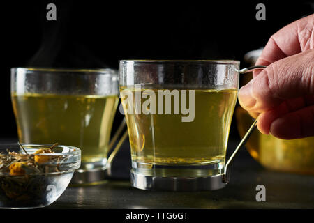 Cropped hand of man holding chamomile tea on table against black background Stock Photo