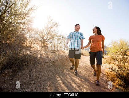 Happy couple walking on dirt road against clear sky Stock Photo