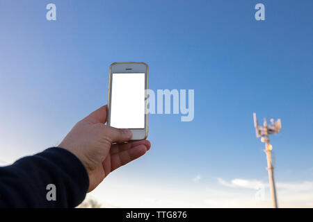 Man holds mobile phone on hand pointing to telephony antenna Stock Photo