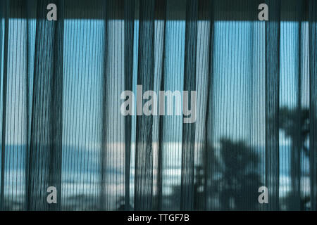 Mesh curtain drawn across window of hotel room overlooking the ocean Stock Photo