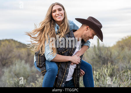 Western wear young couple giving piggy back ride on ranch Stock Photo