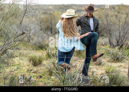 Western wear young couple on desert ranch by barbed wire fence Stock Photo