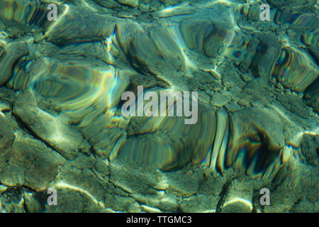 Top view of blue, green and turquoise colors of water, surface of sea on rocks and bottom. Reflection of sun beams in water, shallow soil, shoal. Stock Photo
