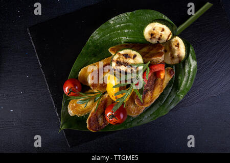 Overhead view of grilled halloumi cheese with cherry tomatoes, peppers and zucchini served in leaf on table Stock Photo