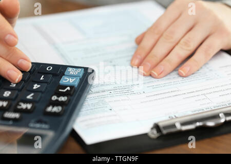 Female hand holding a pen and using calculator while filling in the individual income tax return, close up Stock Photo