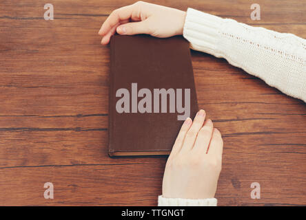 Female hands holding a brown book cover on the brown wooden desk, close up Stock Photo