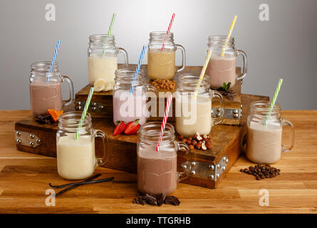 Various types of colouful milkshake and ingredients in Mason Jar glasses with paper straws on a wooden table top Stock Photo
