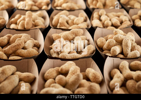 Peanuts with shell in disposable cardboard boxes on a black table. Stock Photo