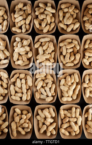 Peanuts with shell in disposable cardboard boxes on a black table. Stock Photo