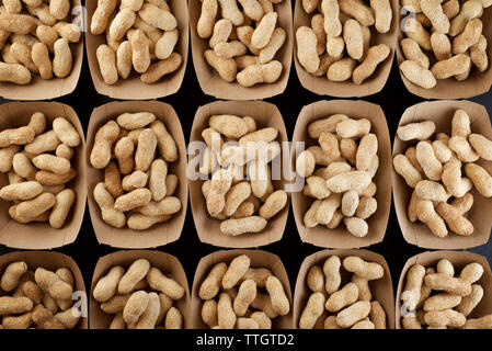 Peanuts with shell in disposable cardboard boxes on a black table. Stock Photo