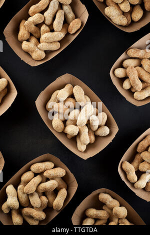 Peanuts with shell in disposable cardboard boxes on a black table. Stock Photo