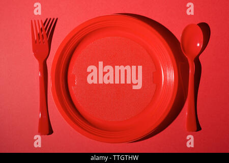 Red disposable plastic cutlery on a red table. Stock Photo