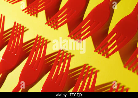 Red disposable plastic cutlery on a yellow table. Stock Photo