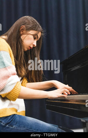 Concentrated young woman playing music on piano in concert hall. Stock Photo