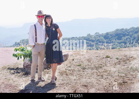 Portrait of newlywed couple standing on mountain against sky during sunny day Stock Photo