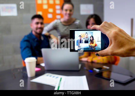 Cropped hand of businesswoman photographing colleagues with mobile phone in board room Stock Photo