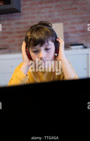 Boy using headphones and laptop computer while studying at home Stock Photo