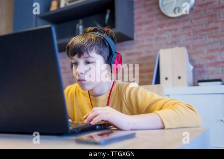 Focused boy learning using laptop computer and headphones at home Stock Photo