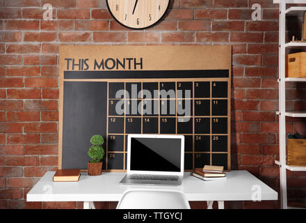 Workplace with laptop, table and calendar board on brick wall background Stock Photo