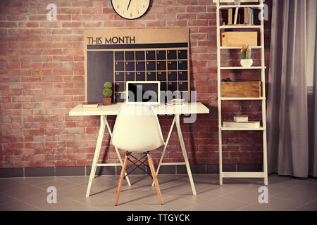 Workplace with laptop, table and calendar board on brick wall background Stock Photo