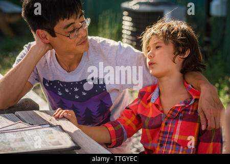 Father and son talking while sitting at wooden table in yard Stock Photo