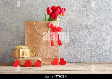 Red tulips in paper bag on wooden table against the grey wall, close up Stock Photo