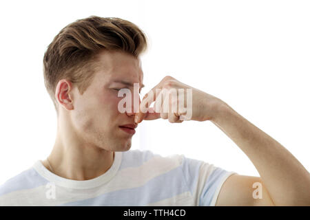 Young blonde man pinching his nose because of the stench, isolated on white Stock Photo