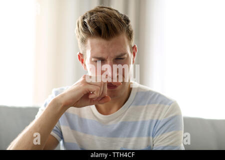 Young blonde man pinching his nose because of the stench in the room Stock Photo