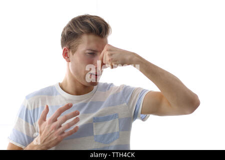 Young blonde man pinching his nose because of the stench, isolated on white Stock Photo