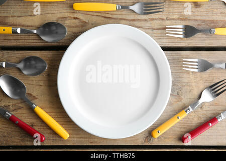 Plate and colorful flatware on wooden table, top view Stock Photo