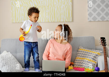 Young woman in headphones and little boy playing with toy saxophone. Stock Photo