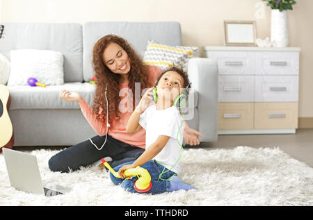 Young woman in headphones listens little boy playing on toy saxophone. Stock Photo