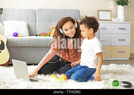 Young woman in headphones listens little boy playing on toy saxophone. Stock Photo