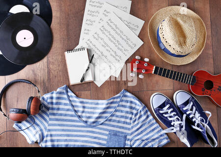 Guitar, headphones, music sheets and clothes on wooden surface, top view Stock Photo