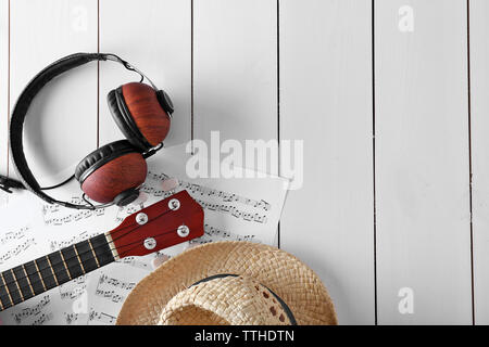 Small guitar, headphones, music sheets and straw hat on wooden surface, top view Stock Photo