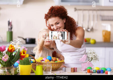 Mother and daughter making selfie while decorating Easter eggs in the kitchen Stock Photo