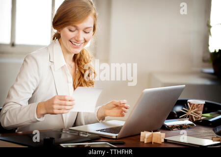Happy photo editor holding photograph while working on laptop at desk Stock Photo