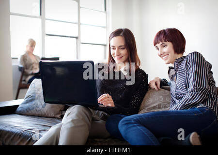 Happy businesswomen working on laptop while sitting on sofa in office Stock Photo