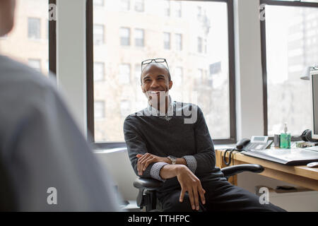 Happy businessman looking at coworker while sitting in office Stock Photo