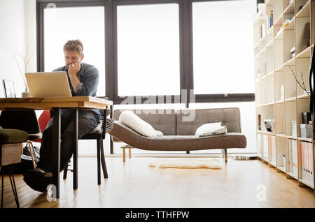 Concentrated man using laptop while sitting at table Stock Photo
