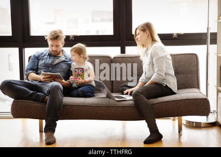 Family using technologies while sitting on sofa at home Stock Photo