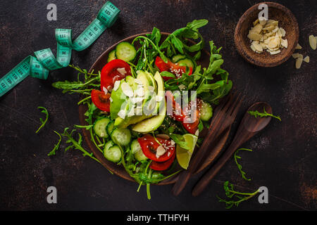 Green salad with avocado, tomatoes, cucumbers and nuts in a wooden plate, a centimeter on a dark background. Fitness and diet food concept. Stock Photo