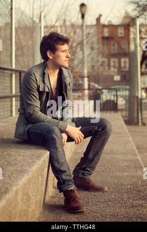 Thoughtful man sitting on retaining wall in city Stock Photo