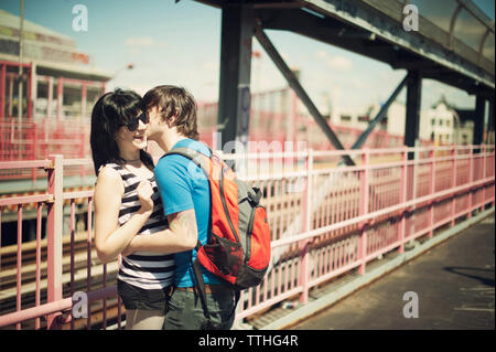 Man kissing girlfriend while standing at bridge on sunny day Stock Photo