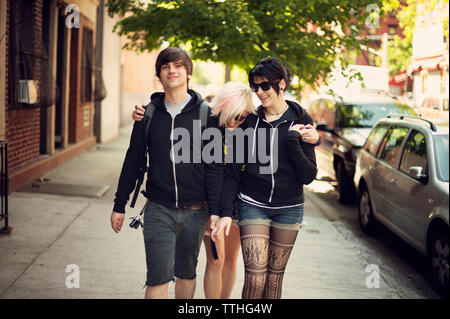 Happy friends walking on sidewalk in city Stock Photo