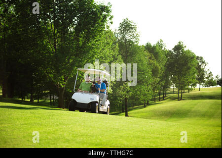 Male golfers driving golf cart on field Stock Photo
