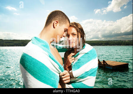 Romantic couple wrapped in towel against lake Stock Photo