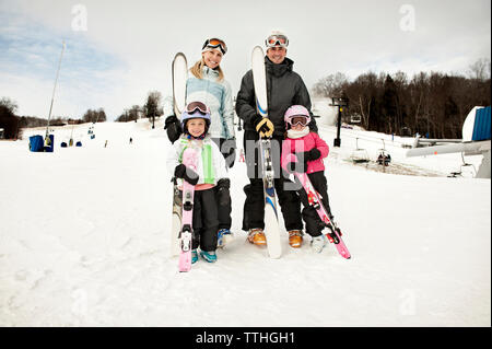 Portrait of happy family holding skis on snow covered field against sky Stock Photo