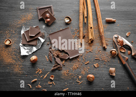 Pieces of chocolate with hazelnuts, cracker and cinnamon on black wooden background Stock Photo