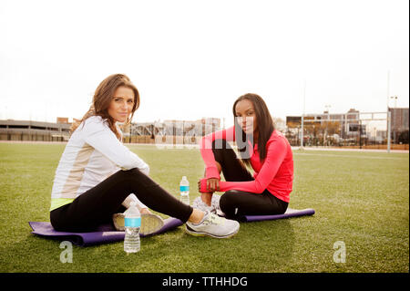 Smiling friends relaxing on grassy field against clear sky Stock Photo